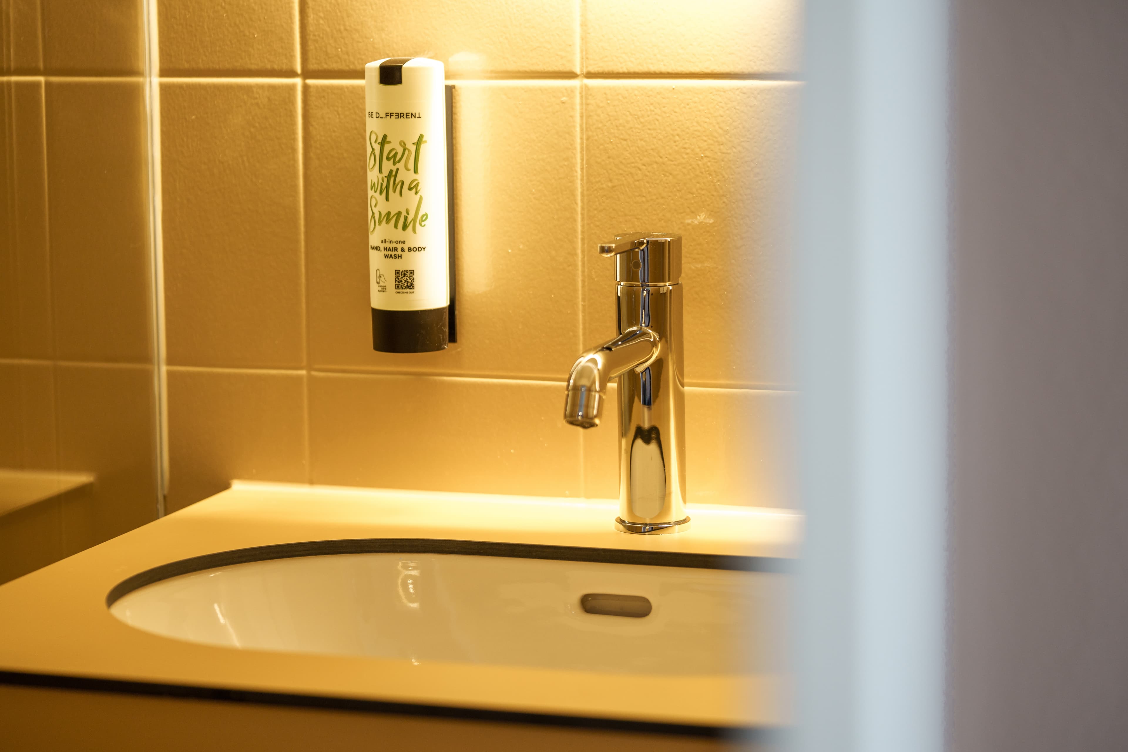 A sink with a faucet and a soap dispenser labeled Start with a Smile in a bathroom.