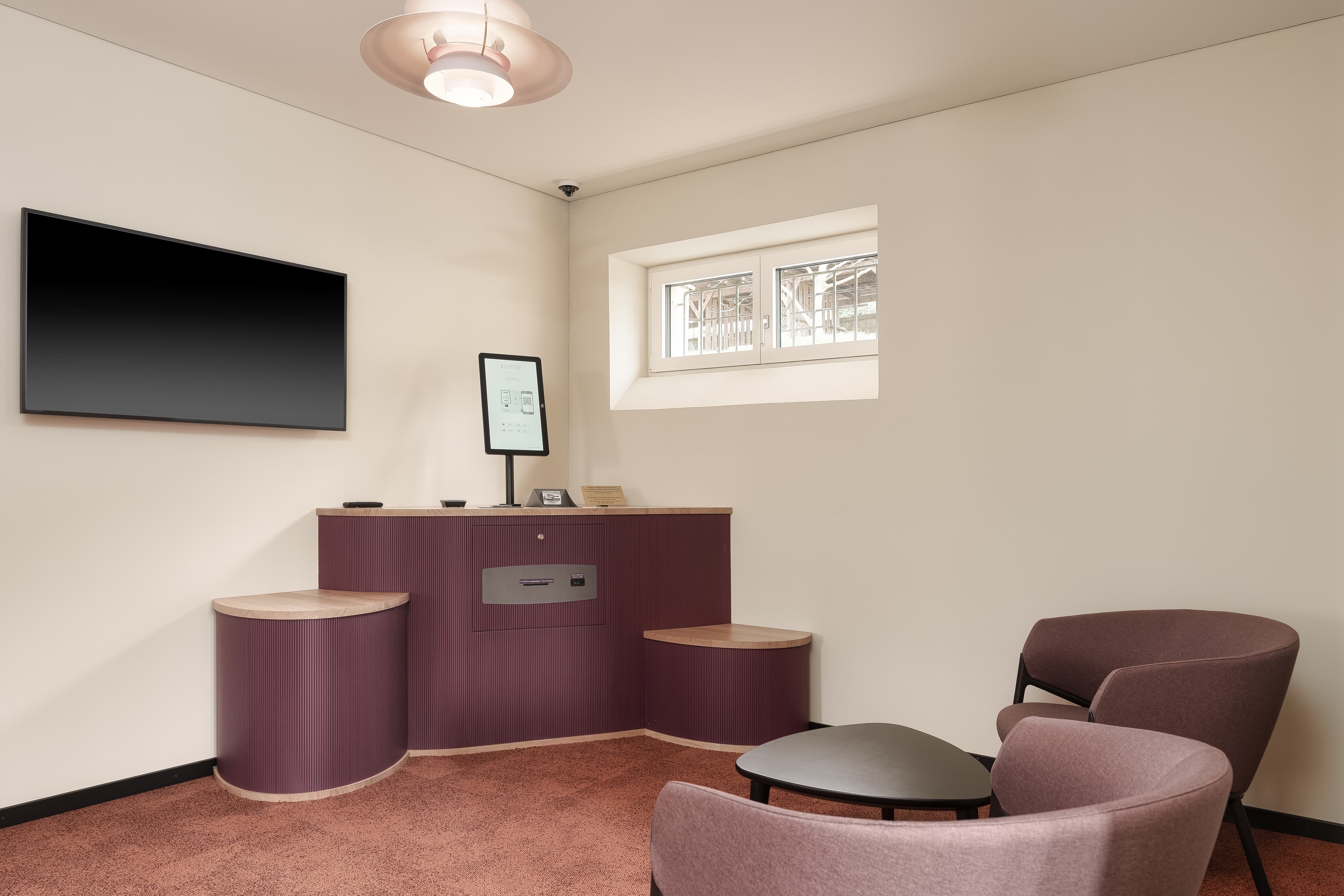 A modern self-check-in area in a monastery with a screen on a reception counter and two armchairs.